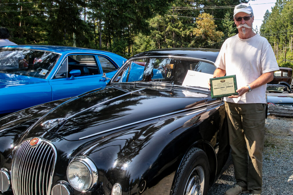 Robert McMillin standing with his black 1959 Jaguar.